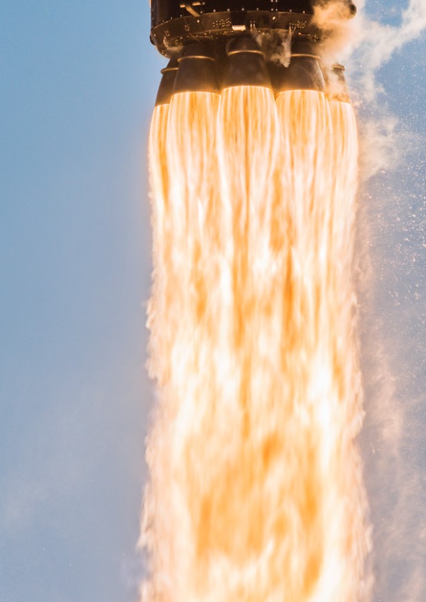 A SpaceX Falcon 9 rocket lifts off and leaves a trail of flames below.